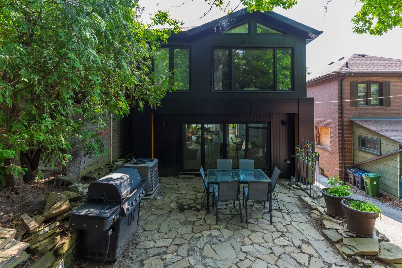Renovated rear exterior with black siding, large glass doors and stone patio