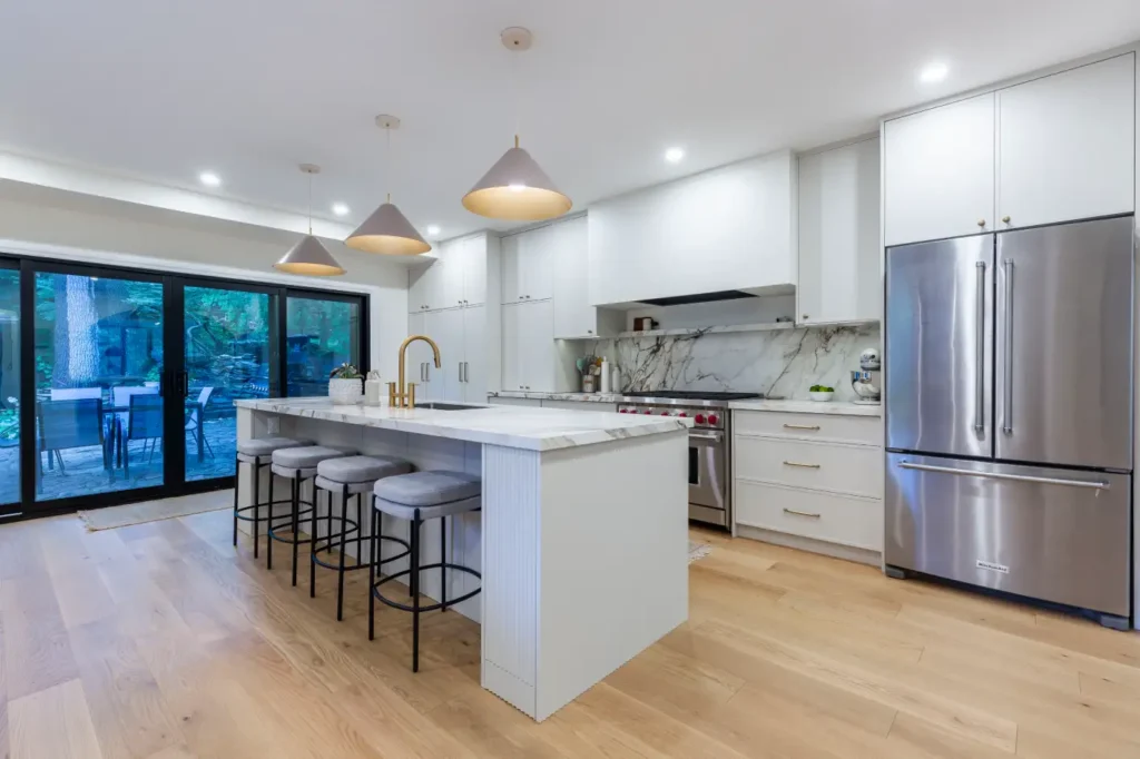 White kitchen with marble backsplash, large island and walkout to the backyard