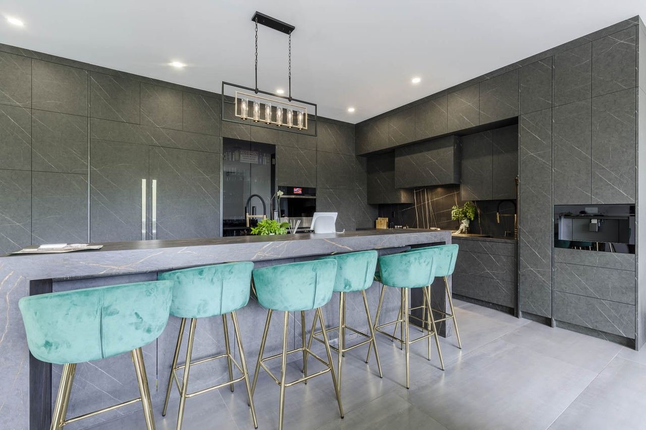 Full width kitchen with long dark stone island and teal bar stools