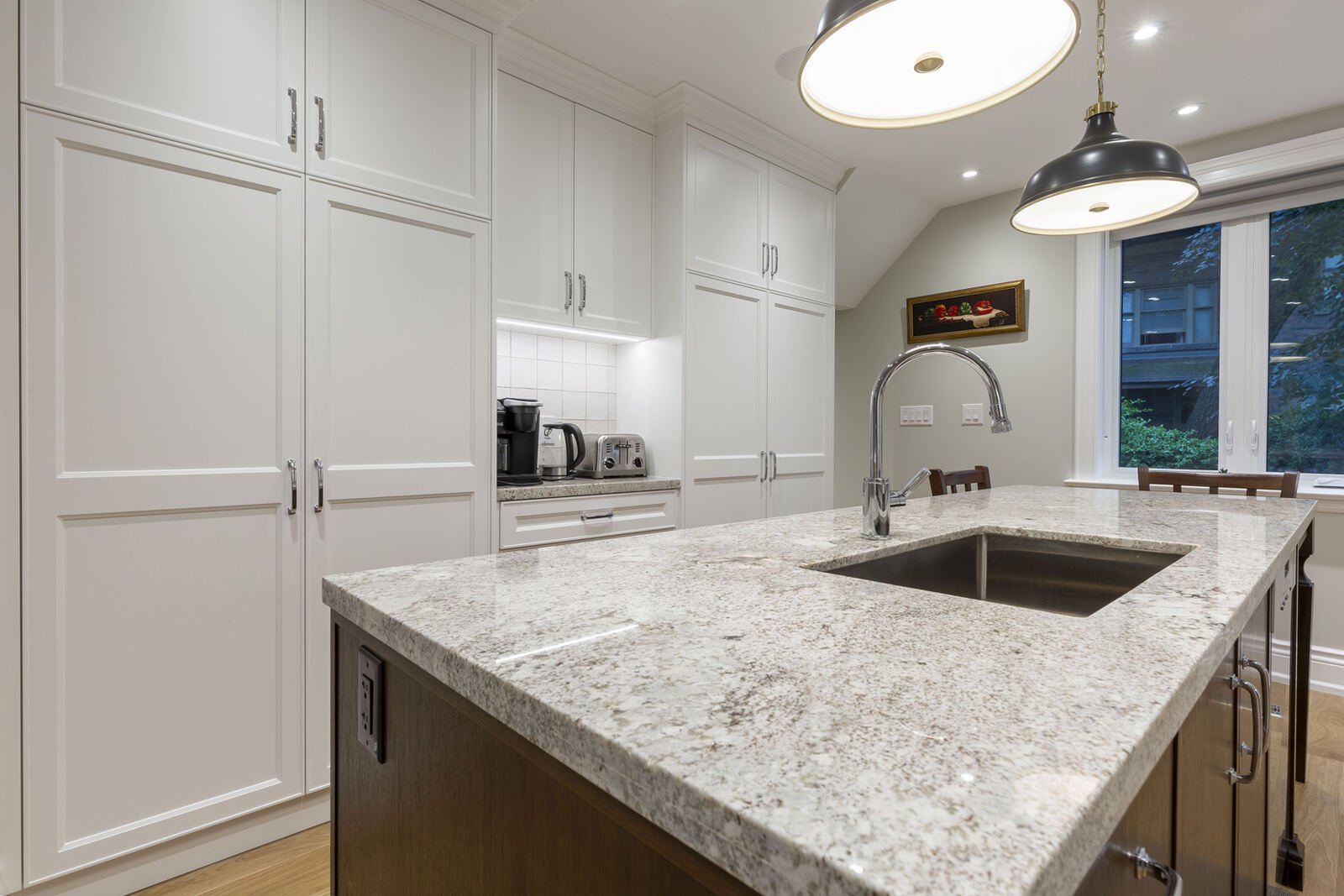Renovated kitchen with granite island, undermount sink and white custom cabinetry