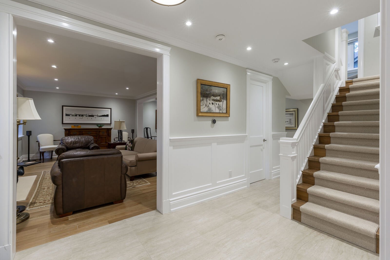 Renovated lower level hallway with wainscoting, travertine tile and carpeted staircase
