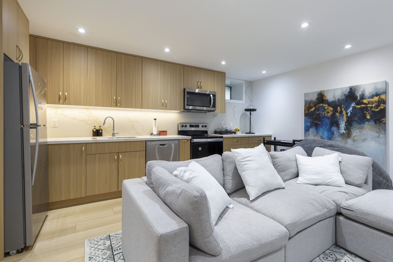 Basement suite with full kitchen, grey sectional and abstract artwork