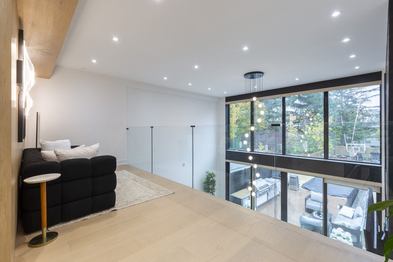Upper loft lounge with black boucle sofa and glass mezzanine railing overlooking the backyard deck