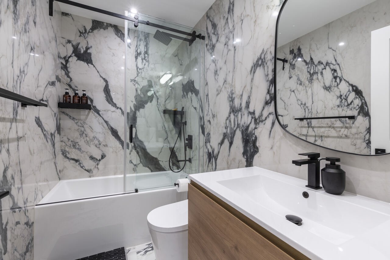 Marble bathroom with tub and shower combination, wood vanity and matte black fixtures