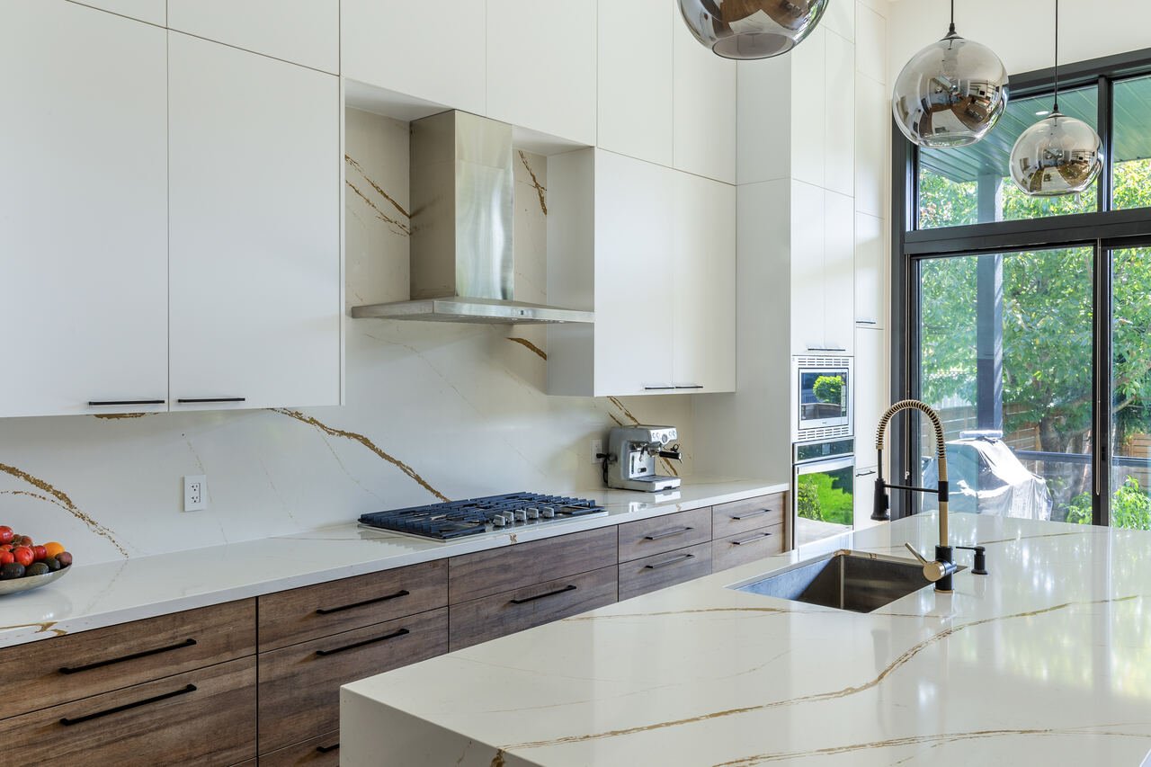 Kitchen with gold-veined quartz counters and backsplash, walnut lower cabinets and gas cooktop