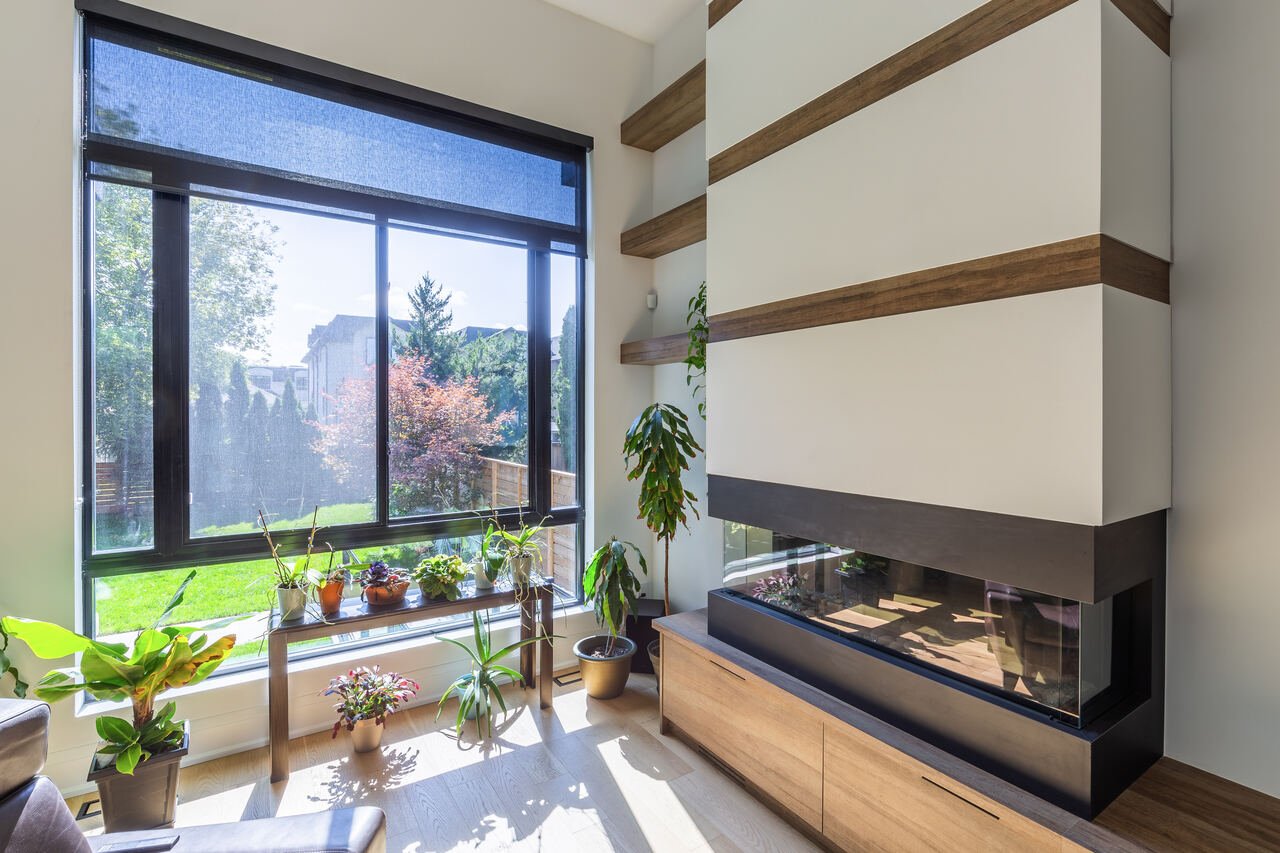 Living room with three-sided gas fireplace, wood accent shelves and floor-to-ceiling windows