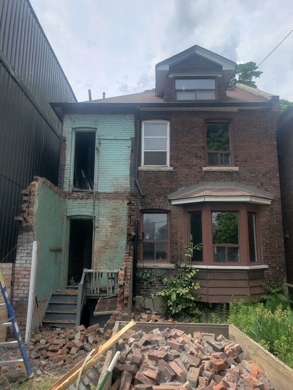 Rear of the original house during demolition with brick removed and salvage piled in the yard