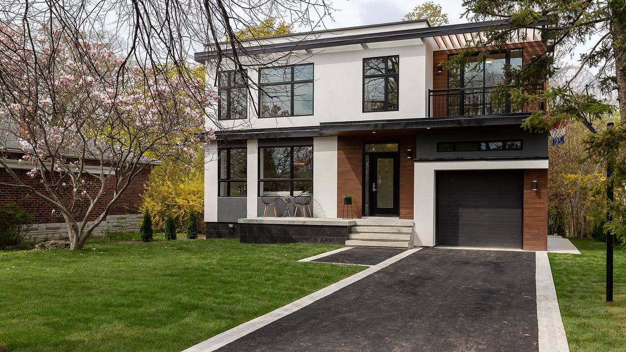 Modern custom-built home front exterior with white stucco, black aluminum windows and wood accents in Etobicoke