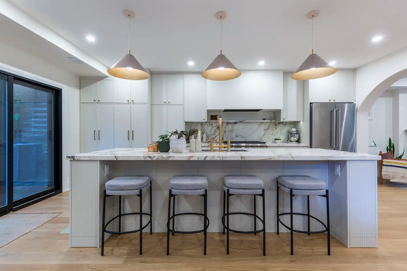 Renovated kitchen with marble waterfall island, brass fixtures and pendant lighting