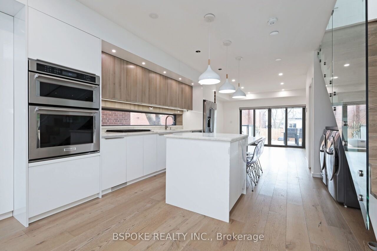 Open kitchen with white island, pendant lights and glass staircase