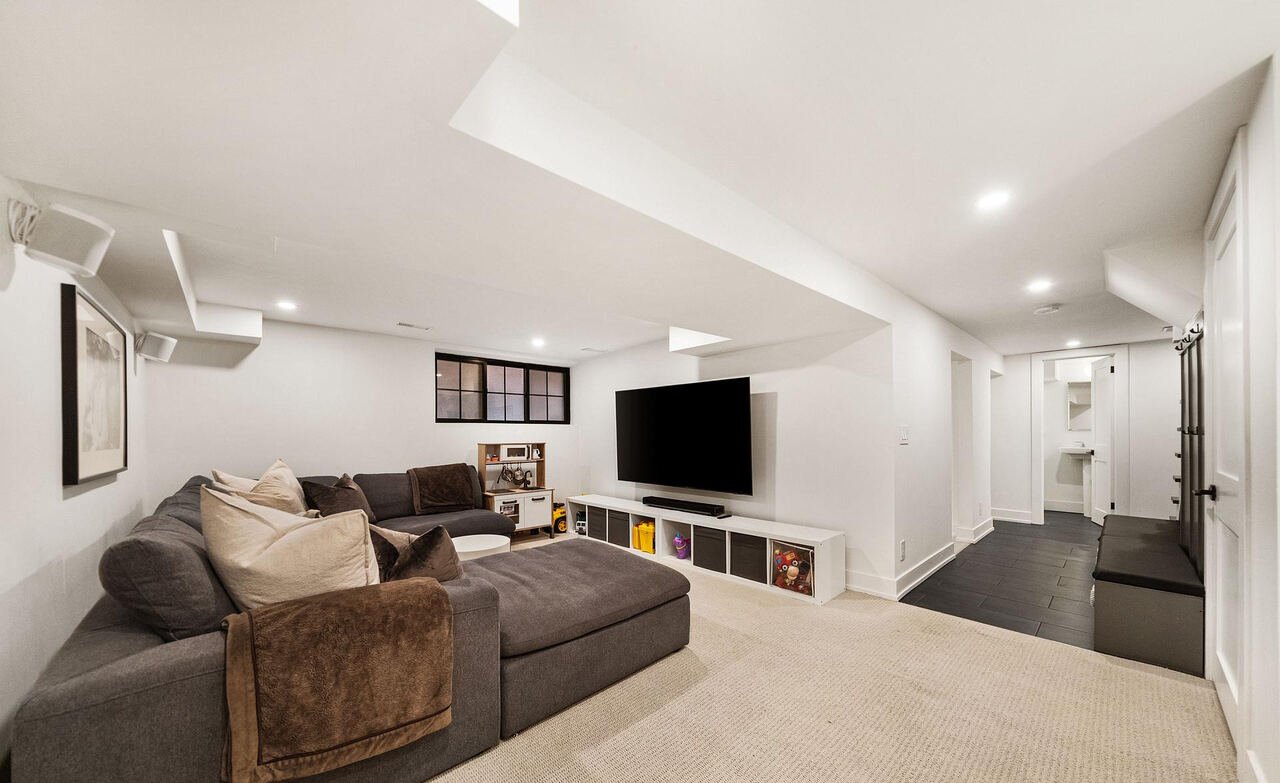 Finished basement recreation room with sectional sofa, wall-mounted television and play area