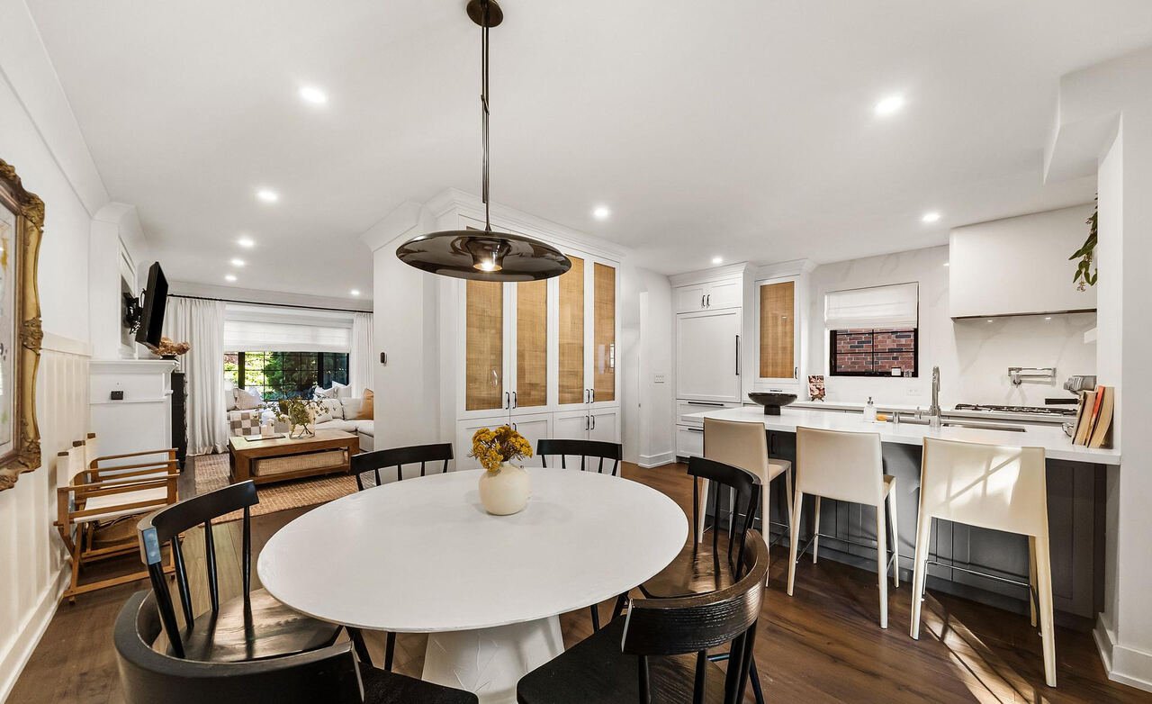 Round dining table with black chairs, open to the kitchen island and bar seating beyond