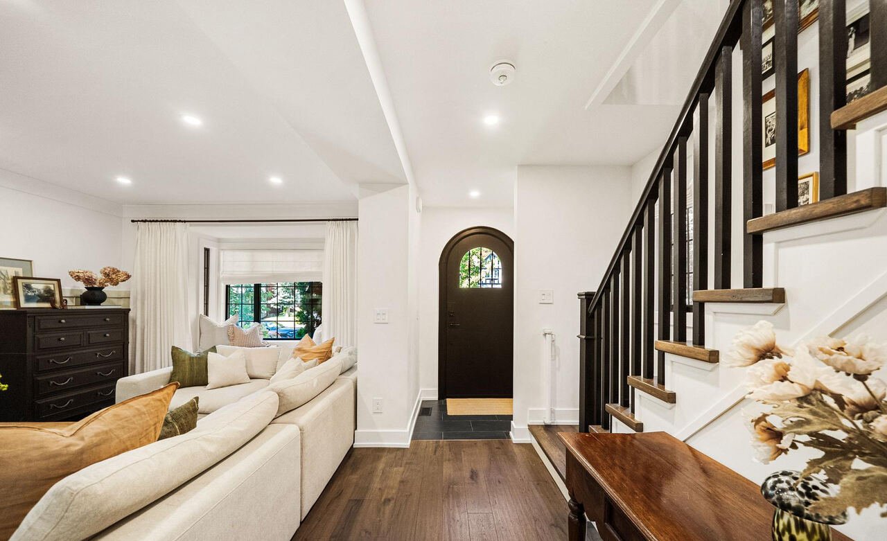 Open entry hall looking toward the arched front door, with living room and dark-stained staircase alongside