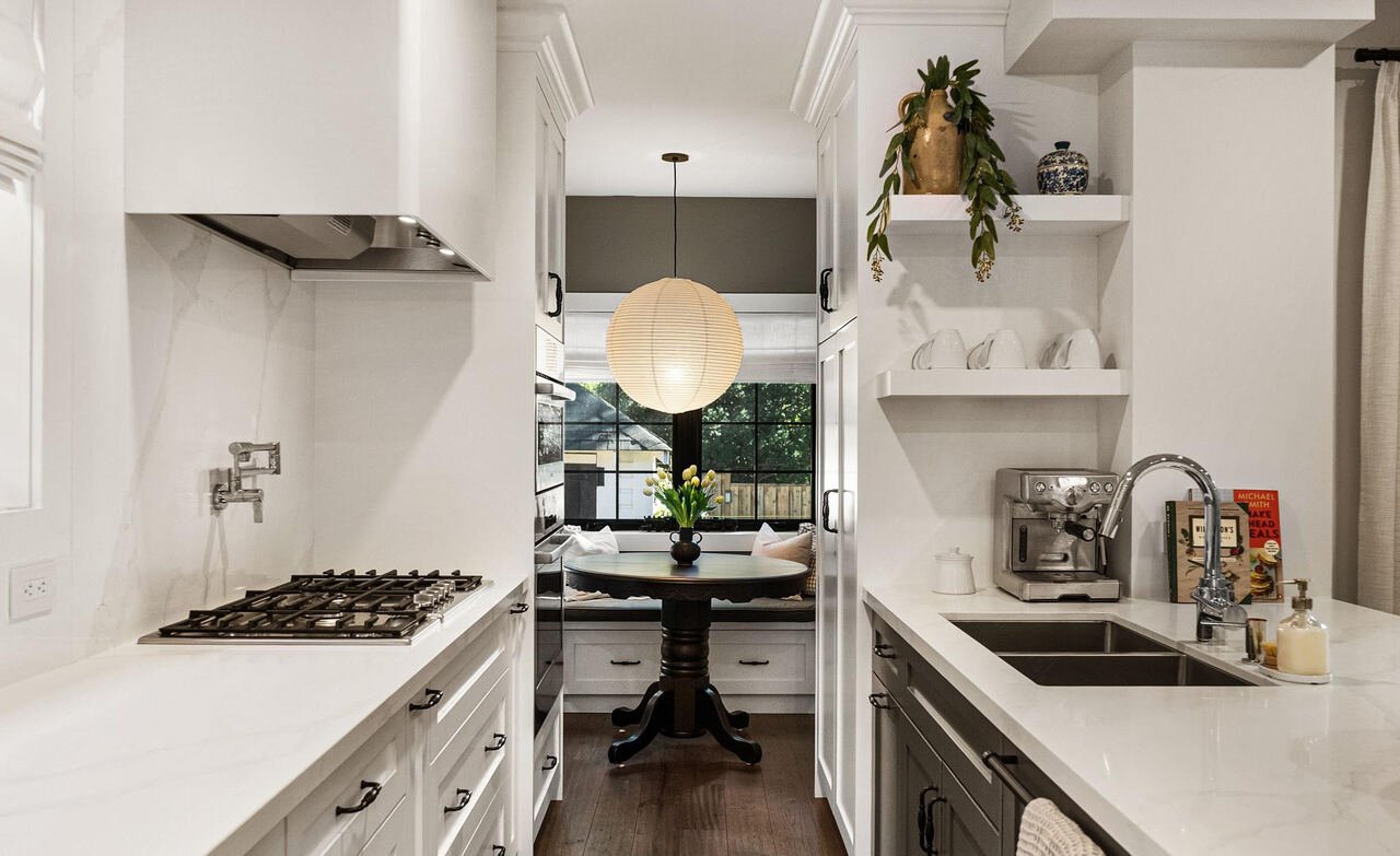 Galley kitchen with gas cooktop, pot filler, marble countertops and paper lantern pendant over the breakfast nook