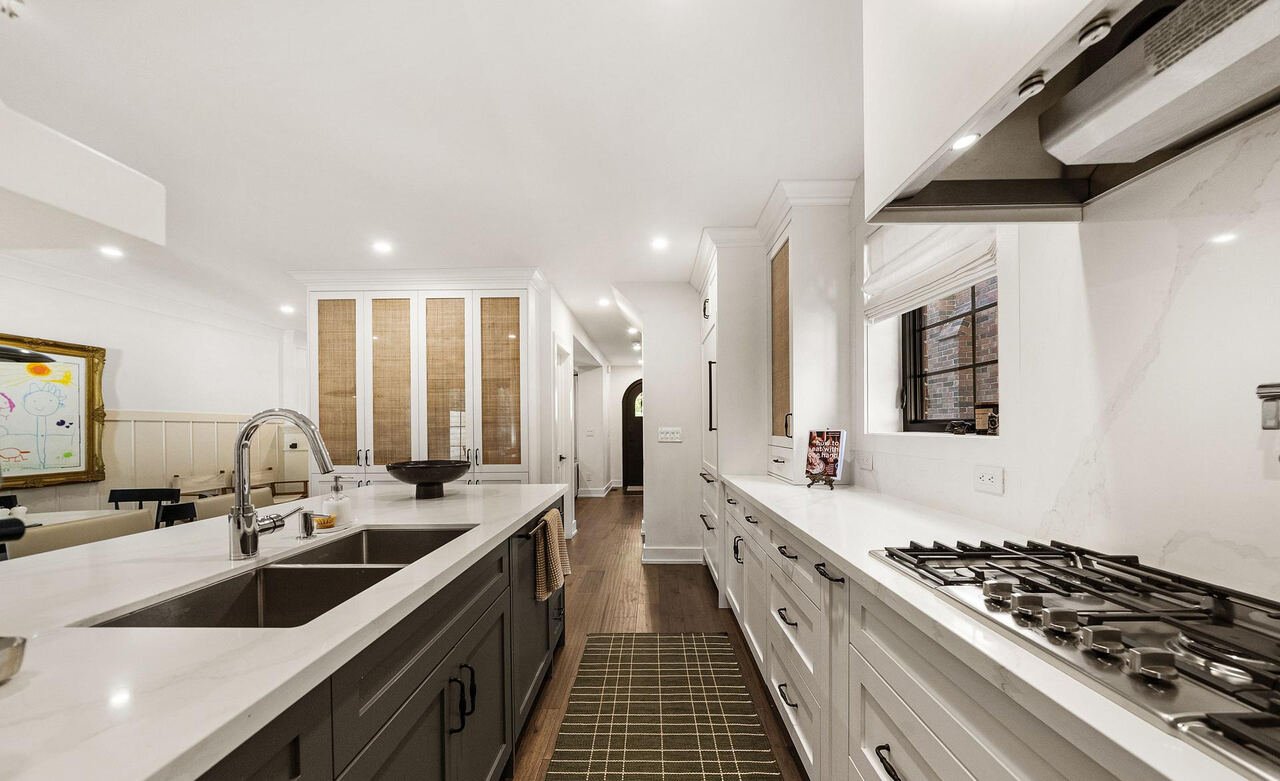 Kitchen work aisle with gas range, undermount sink and floor-to-ceiling rattan-front pantry cabinetry