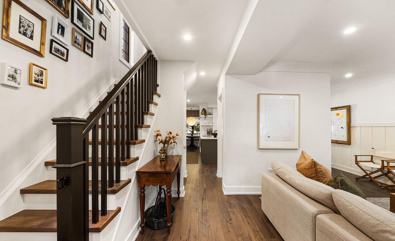 Dark-stained staircase with family photo gallery wall, looking through the open main floor toward the kitchen
