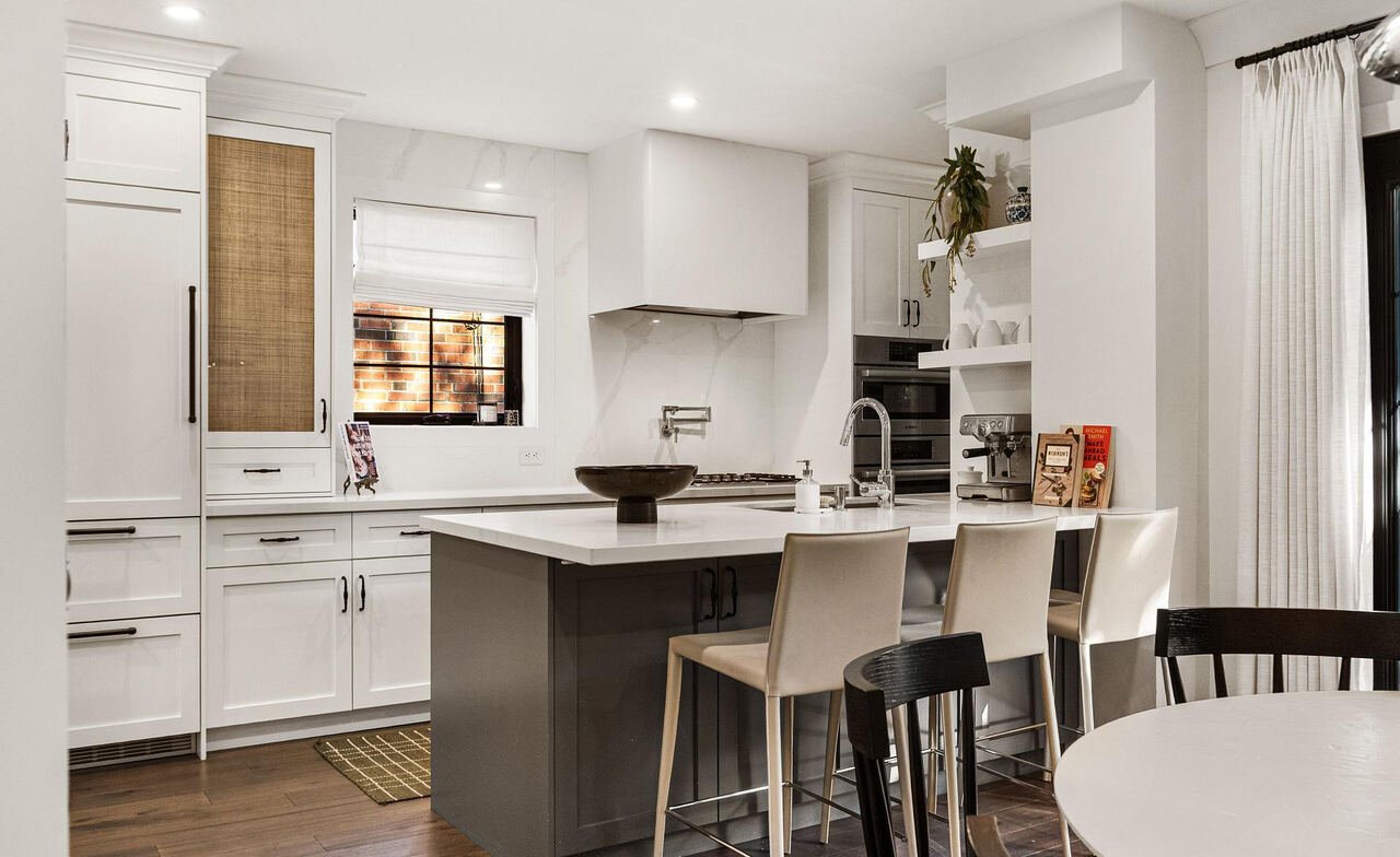 White shaker kitchen with rattan cabinet inserts, grey island, marble backsplash and bar seating