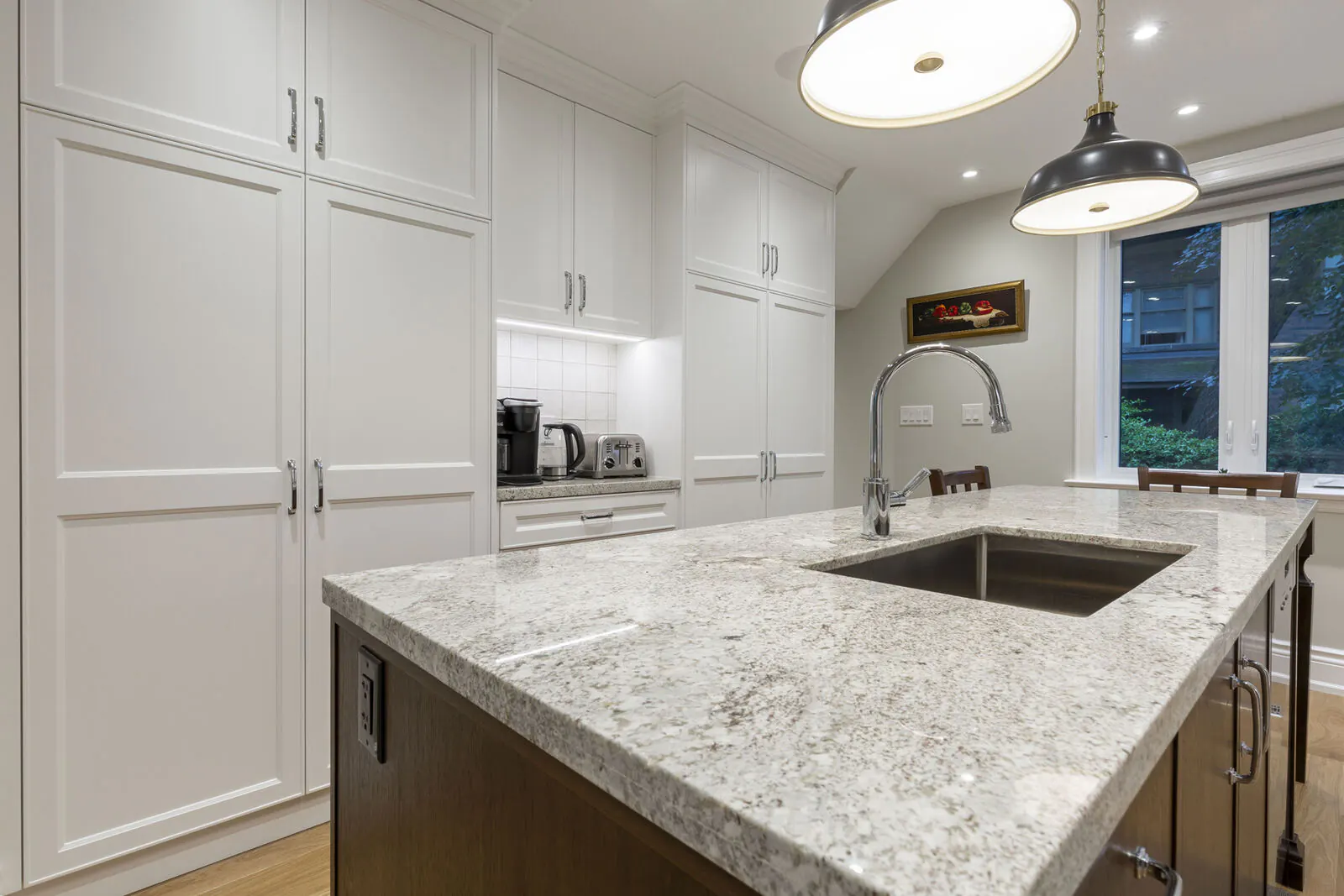 Renovated kitchen with granite island, undermount sink and white custom cabinetry